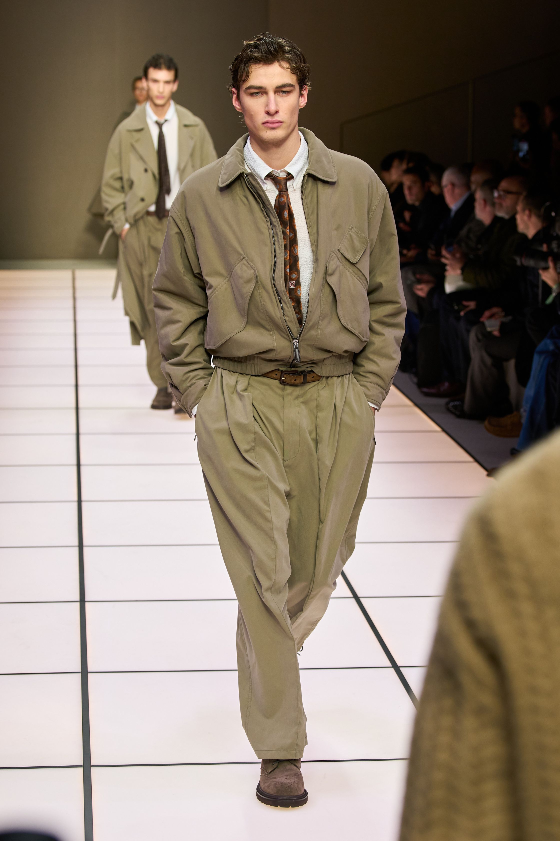Giorgio Armani 26FW 男装回归品牌最本质的语言：流动、克制与永恒。柔软大衣、宽松长裤、针织与轻结构西装在灰、驼、米与墨绿中缓慢展开，强调身体与面料之间的自然关系。系列几乎不依赖任何戏剧化装饰，却通过比例、步伐与质感建立权威感，是对“真正优雅无需证明”的再次确认，也是一种对快节奏时尚的温和抵抗-顽石频道趋势研究